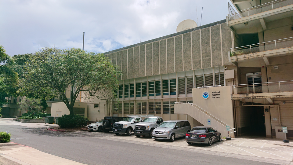 Photograph of the outside of the NWS office in the HIG building. The external staircase with a NOAA logo leads to the second floor, with the office entrance at the top of the stairs. An elevator is available through the corridor to the right of the staircase.